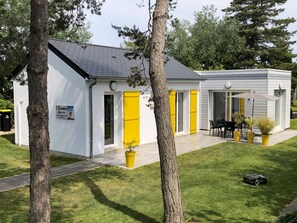 A modern building with a white exterior, yellow doors, and a patio area with outdoor seating. - Charming house with garden near the beach (Saint-Jean-de-la-Rivière)
