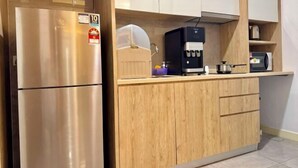 Une cuisine de taille réduite, dotée d’un réfrigérateur en acier inoxydable, d’une machine à café et de meubles de rangement en bois.