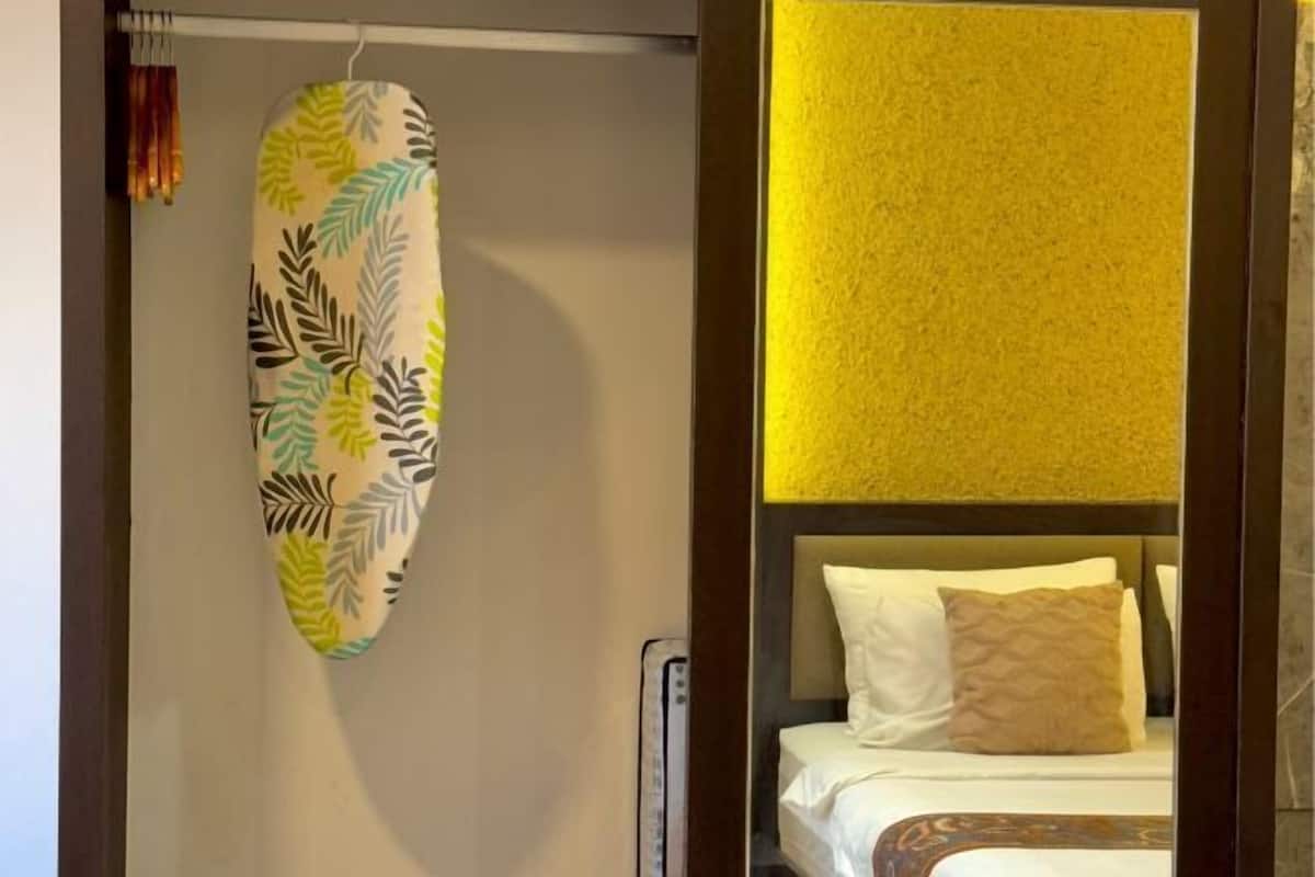 Une chambre d’hôtel avec un lit, une tête de lit et un porte-serviettes fixé au mur, orné d’une serviette à motifs de feuilles.