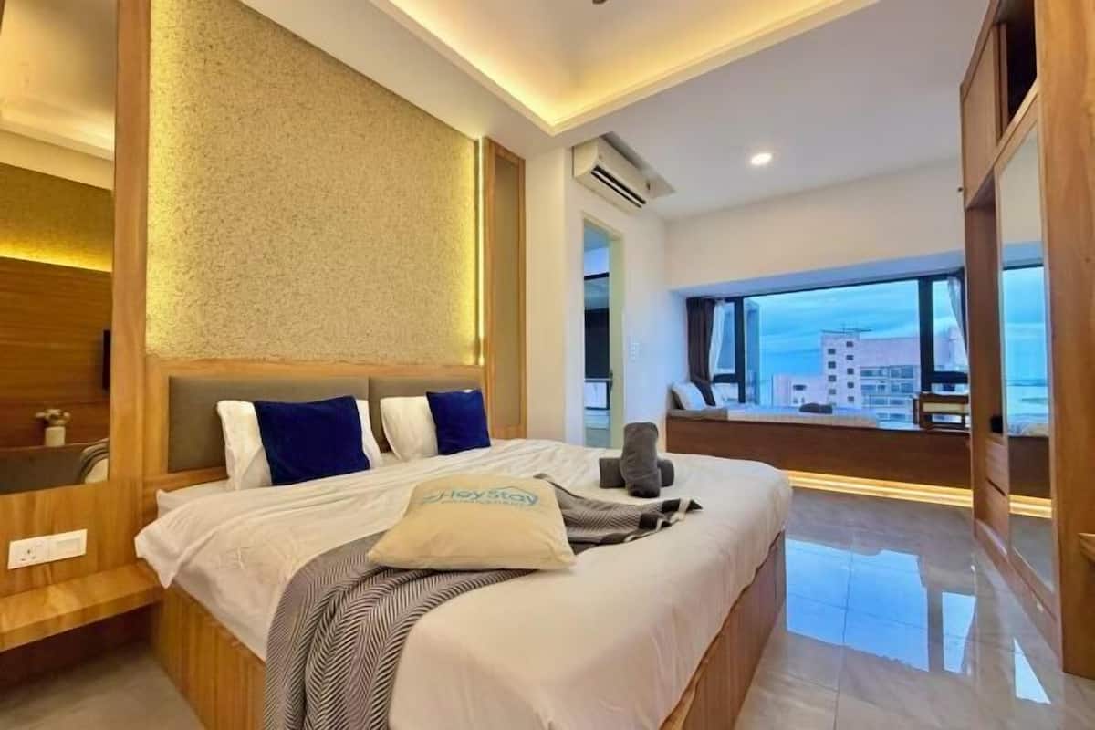 Une chambre d’hôtel avec un grand lit, une tête de lit en bois, une vue sur la ville et une fenêtre.