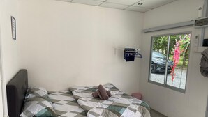 A single bed with a checkered bedspread, a bedside table, and a window with a view of a car and greenery outside. - Capital O 91228 Hureen Chalet Hmk (Arau)