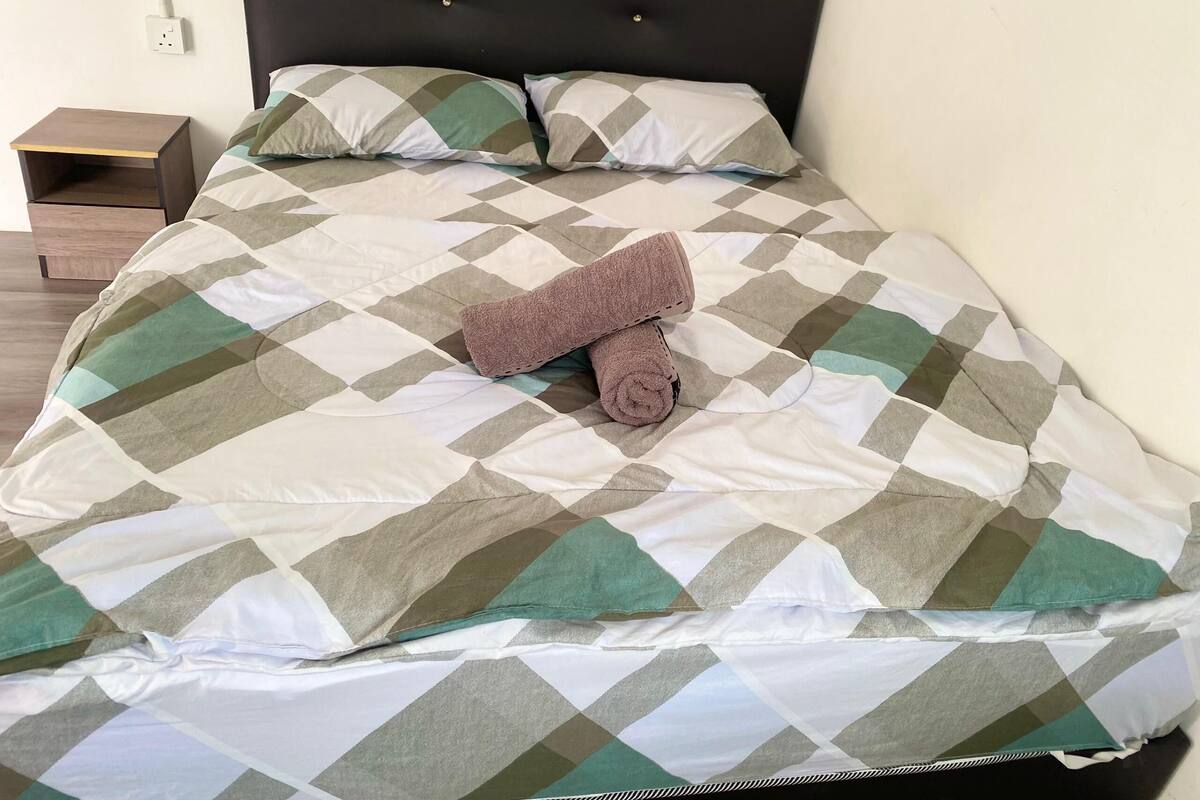Una cama bien hecha con una colcha a cuadros, dos almohadas y una toalla enrollada.