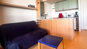 Een knus woongedeelte met een bank, een klein tafeltje, een kitchenette en een houten trap.