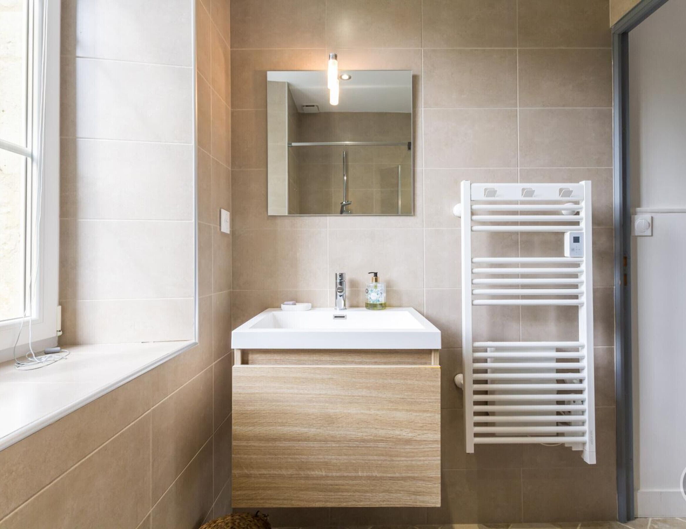A modern bathroom with a white sink, a mirror, a towel rack, and a shower.