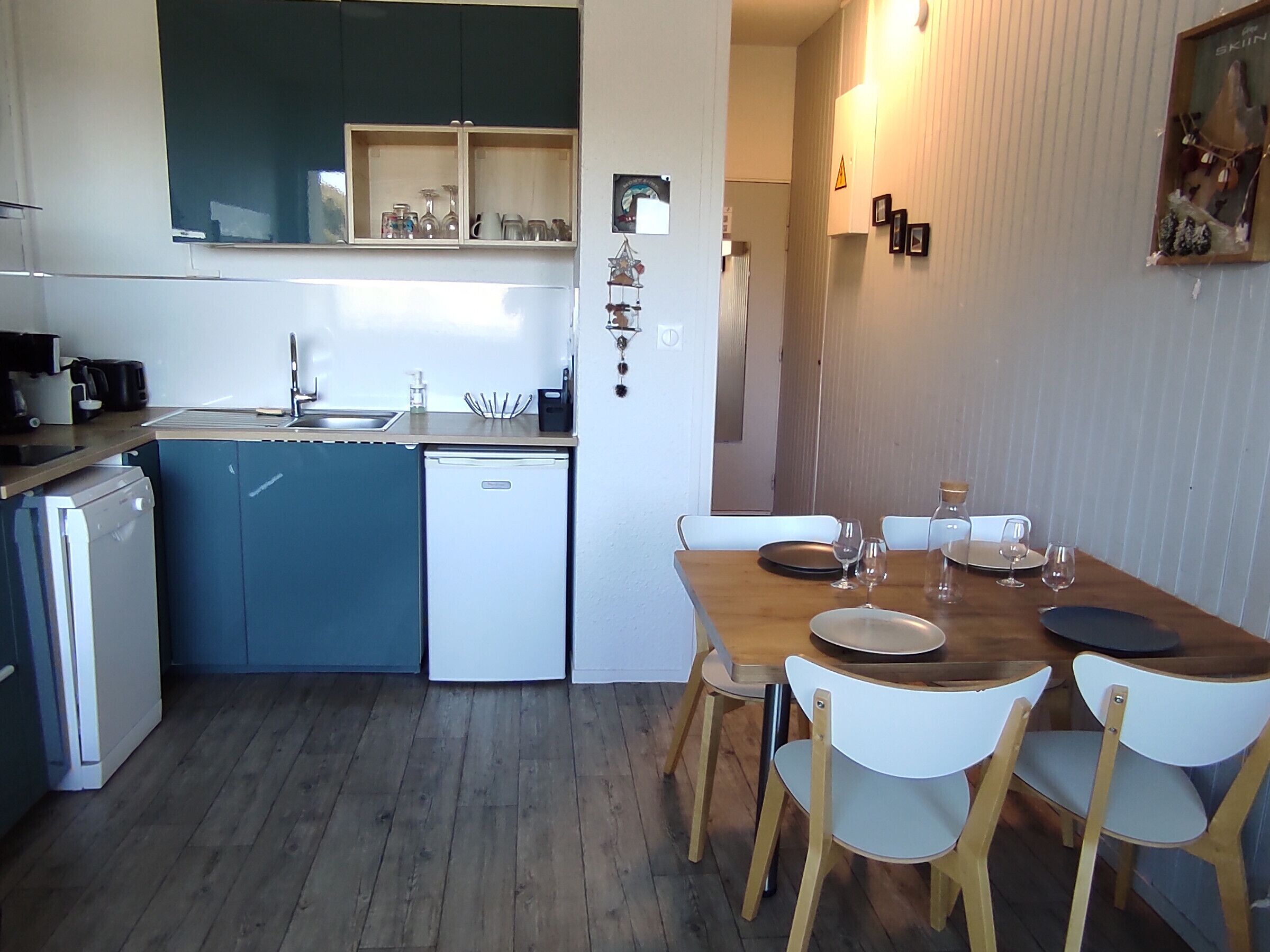 A compact kitchen with a sink, a small refrigerator, and a dining area with a wooden table and white chairs.