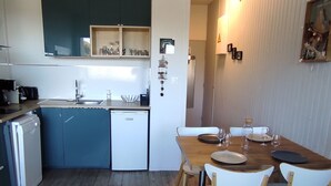 Une cuisine compacte comprenant un évier, un petit réfrigérateur et un coin repas avec une table en bois et des chaises blanches.
