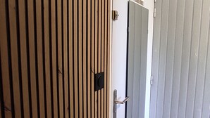 Une porte en bois ornée d’un motif à panneaux verticaux, dotée d’une poignée en métal et d’une petite plaque carrée noire.
