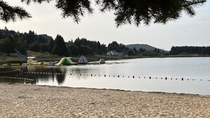 Une plage de sable fin, un lac paisible, des arbres et une colline qui se dessine à l’horizon.