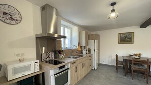 A modern kitchen with stainless steel appliances, a wooden dining table, and a hanging light fixture. - Charming Cottage in Auvergne with Pets Allowed (Bellenaves)