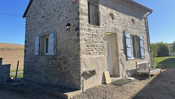 A stone building with a sloped roof, a wooden door, and two windows with shutters. - Charming Cottage in Auvergne with Pets Allowed (Bellenaves)