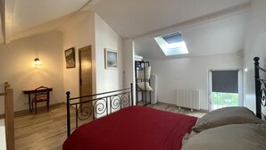 A bedroom with a bed, a skylight, a radiator, a chair, a table, and a door. - Charming Cottage in Auvergne with Pets Allowed (Bellenaves)