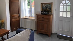 A room with a wooden door, a window with a view, a radiator, a cabinet, and a framed picture on the wall. - Charming Cottage in Auvergne with Pets Allowed (Bellenaves)