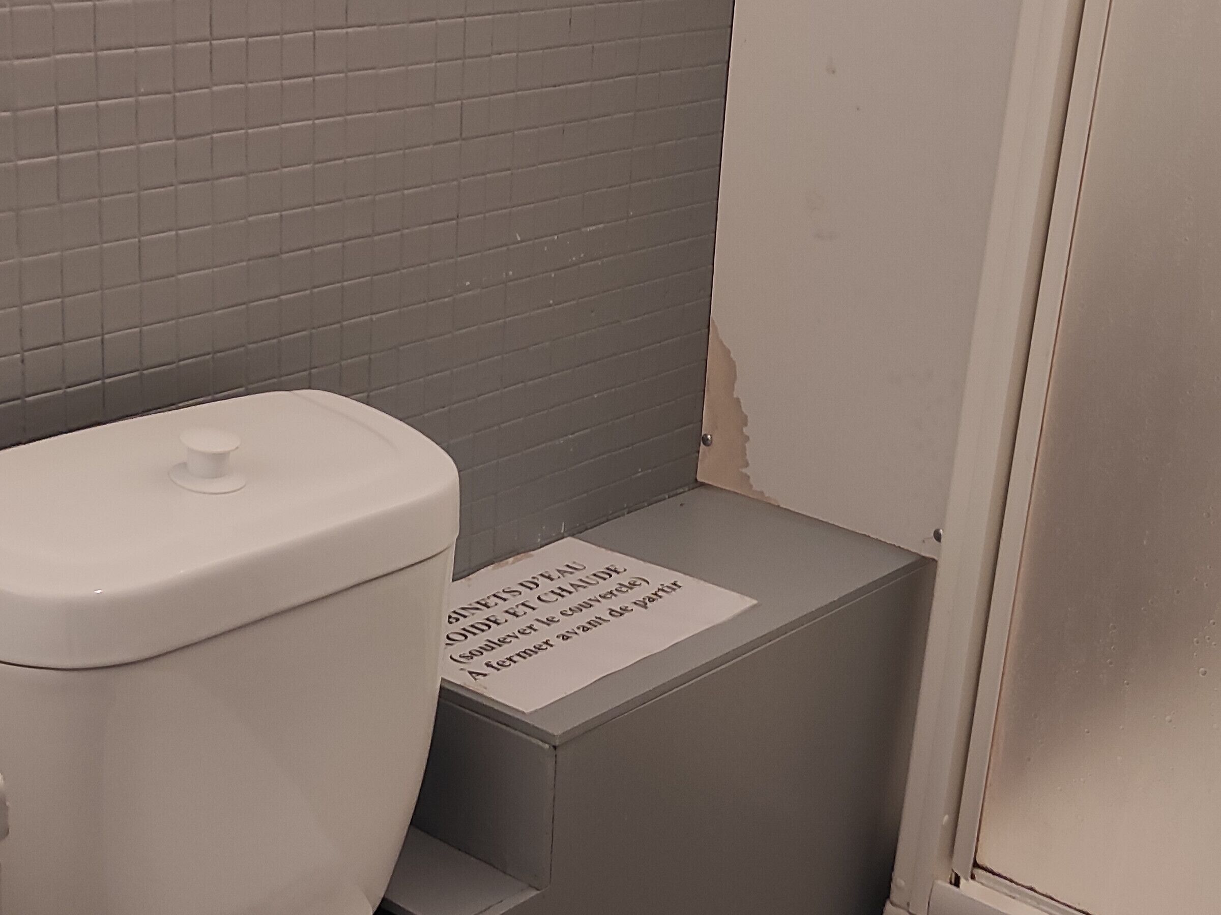 A toilet with a sign in French, a tiled wall, and a door.