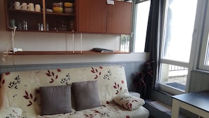 Un salón con un sofá estampado con motivos florales, un armario de madera encima y una ventana con vistas al exterior.