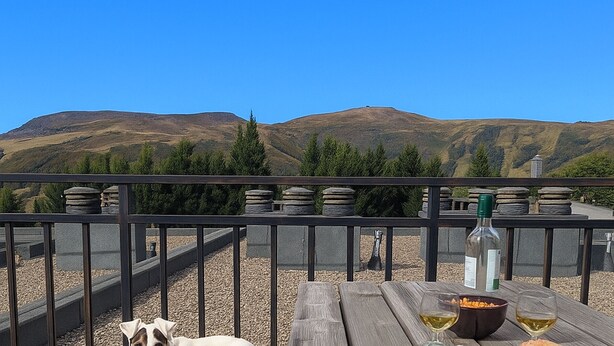 Una terraza de madera con una mesa dispuesta para comer, con vista a un paisaje montañoso.