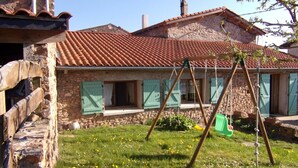 A stone house with a red-tiled roof, a swing set, and a grassy yard with flowers. - Country cottage with pets allowed near Roanne (Neulise)