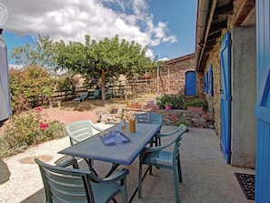A patio with a table and chairs, surrounded by a stone wall and a blue door.
