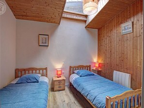 A bedroom with two wooden beds, a skylight, and a wooden wall.