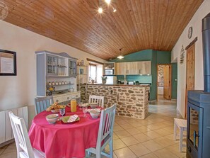 A dining area with a table set for four, a kitchen with a stone island, and a wood-paneled ceiling.
