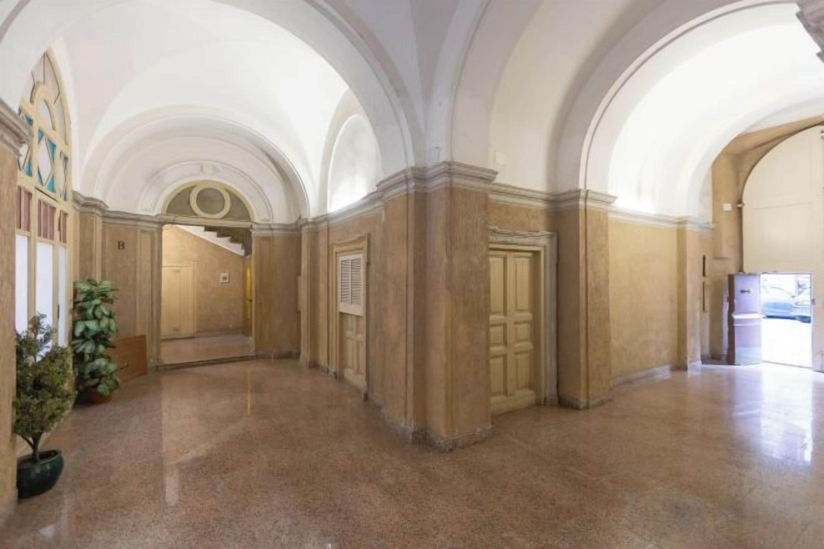 A spacious corridor with arched ceilings and a polished floor, leading to a door at the end.