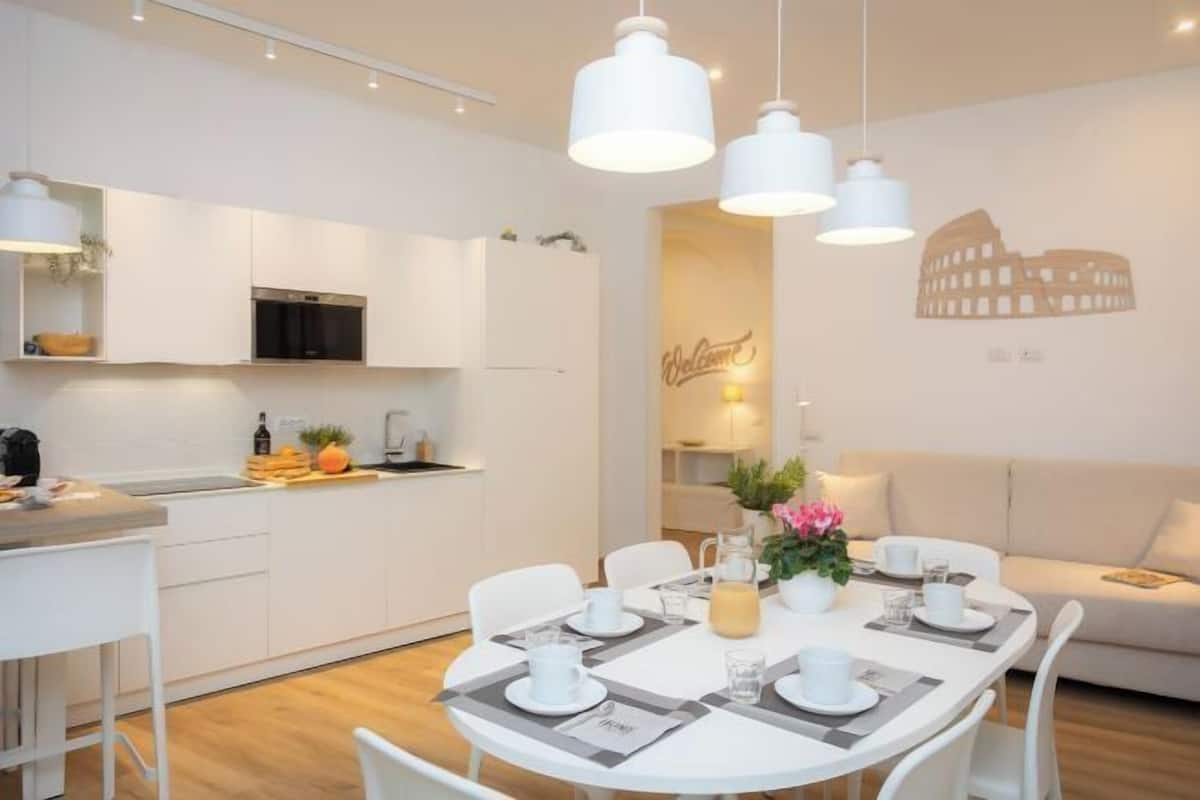 A modern kitchen with white cabinets, a built-in oven, and a dining area with a round table set for four.