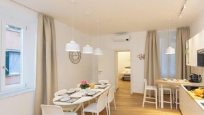Una cocina moderna con electrodomésticos blancos, un comedor con una mesa dispuesta para cuatro personas, y un pasillo que conduce a un dormitorio.