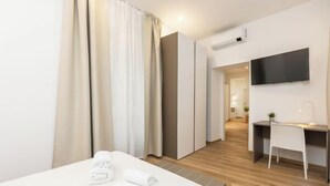 Habitación de hotel con cama, escritorio, silla, televisor y aire acondicionado.