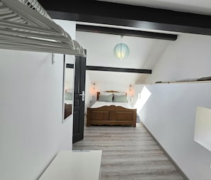 A narrow hallway leading to a bedroom with a wooden bed, white walls, and a skylight.