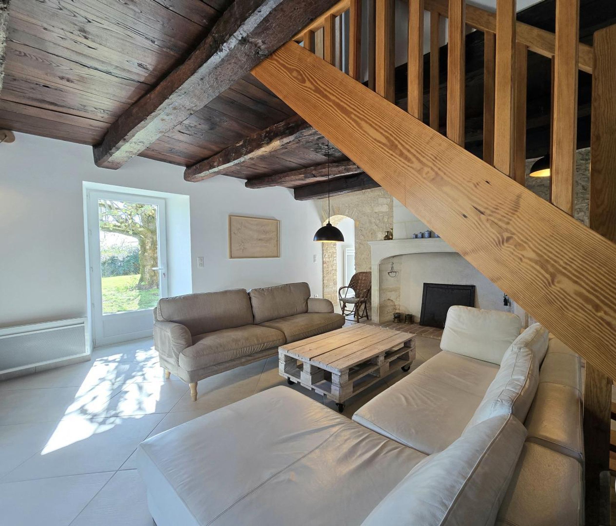 A spacious living room with a wooden staircase, a sofa set, a coffee table, and a fireplace.