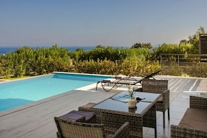 Una piscina con sillones de descanso y una mesa, rodeada de vegetación y vistas al océano.