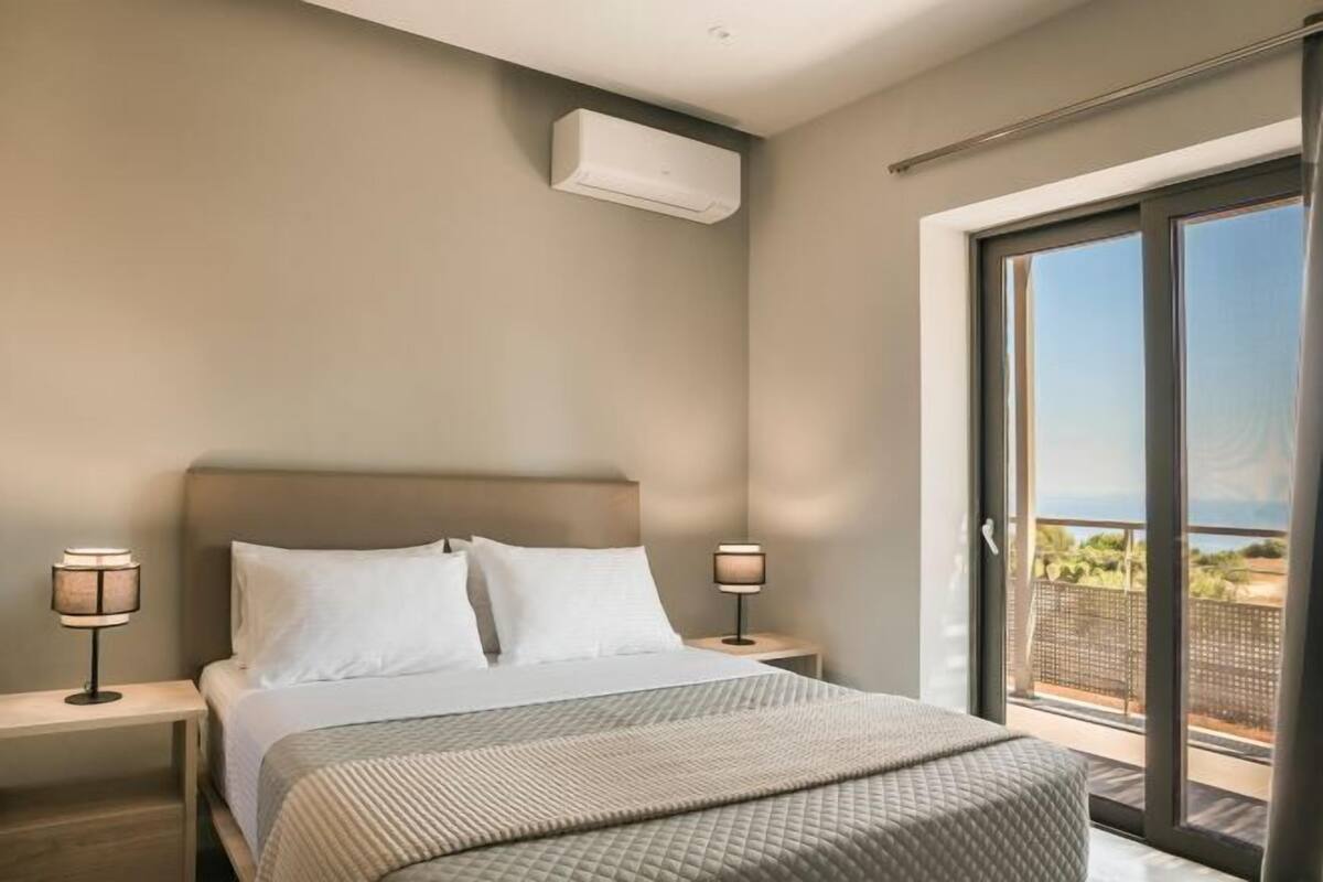 Quarto de hotel com cama, duas luminárias laterais, janela com vista e ar condicionado.