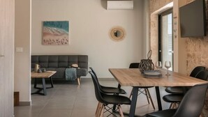 Een moderne woonkamer met een bank, een eettafel met stoelen en een aan de muur bevestigde televisie.