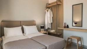 Een tweepersoonsbed met een gewatteerde hoes, een nachtkastje met een lamp, een houten plank met een badjas, en een spiegel aan de muur.