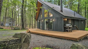 A cabin with a deck, large windows, and a chimney. - The Black Pocono Chalet |  Modern Cabin in Nature (Tobyhanna Township)