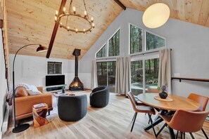 Ein modernes Wohnzimmer mit Kamin, Holzboden und großen Fenstern, sowie einem Essbereich.