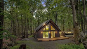 A cabin with a deck, surrounded by a forest. - The Black Pocono Chalet |  Modern Cabin in Nature (Tobyhanna Township)