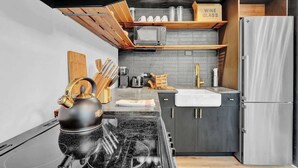A modern kitchen with a black stove, wooden cabinets, a stainless steel refrigerator, and a microwave on a wooden shelf. - The Black Pocono Chalet |  Modern Cabin in Nature (Tobyhanna Township)