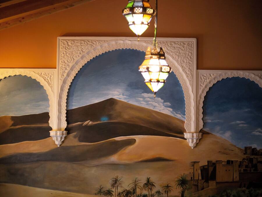 A mural of a desert landscape with architectural arches and a hanging lantern.