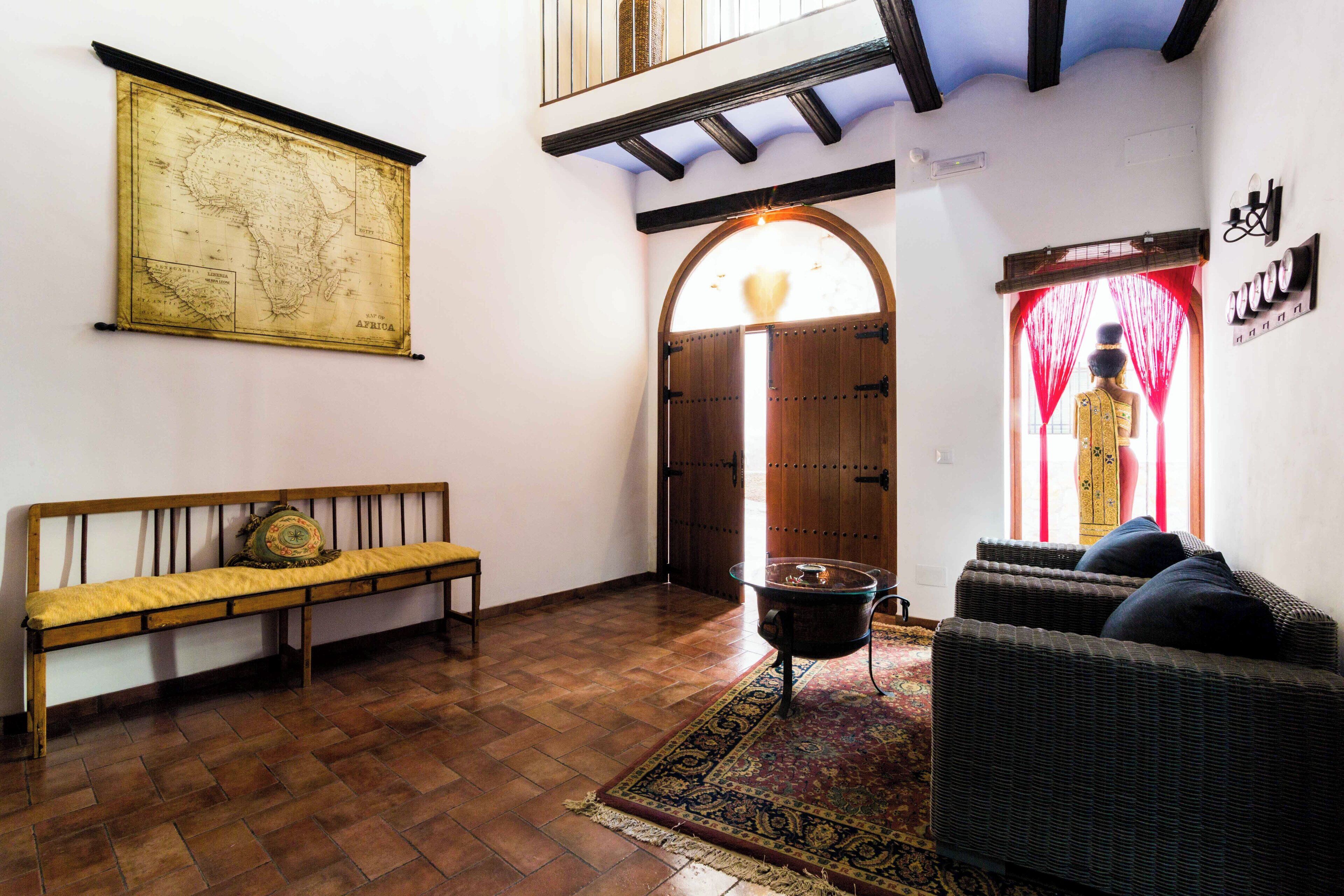 Una habitación con un banco de madera, un sofá de mimbre, un mapa en la pared y una puerta tradicional con cortinas.