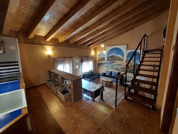 A spacious living area with a wooden ceiling, a sofa set, a dining table, and a staircase. - Alojamientos Mundobriga (Munébrega)