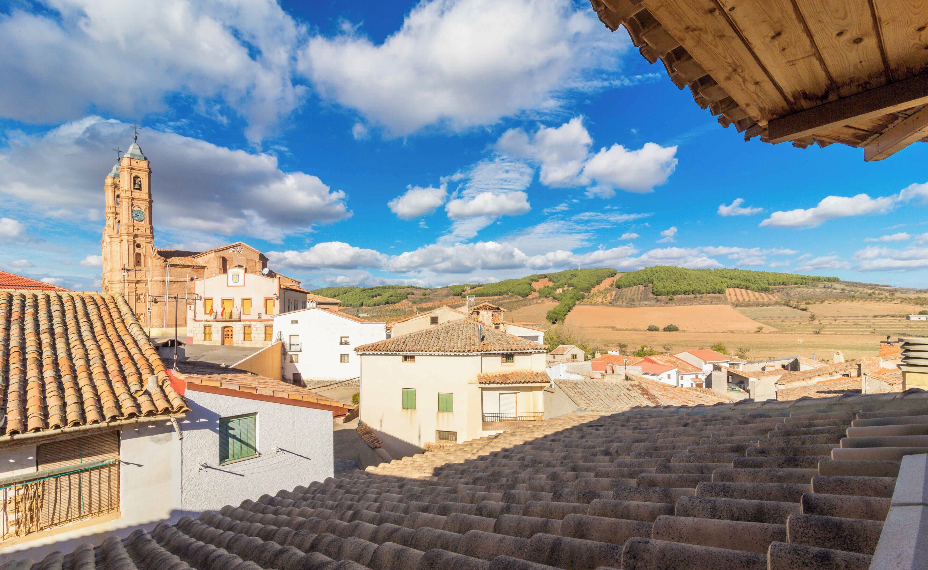 Un pueblo con edificios de tejas de terracota, una destacada torre del reloj y un paisaje montañoso al fondo.
