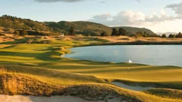 Campo de golfe com lago, bunkers de areia e uma bandeira.