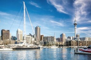 A waterfront cityscape with a prominent tower, a large sailboat, and a marina with several boats. - Point Residence (Auckland)