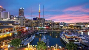 A marina with boats docked, a prominent tower in the background, and buildings with illuminated windows. - Point Residence (Auckland)