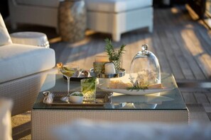 A glass-top table with a tray of food, a glass of drink, and a decorative item on a wicker sofa. - Point Residence (Auckland)
