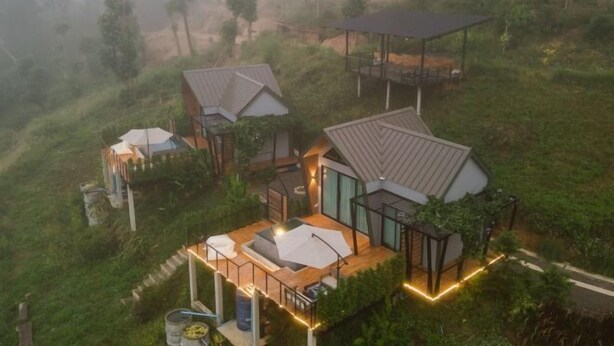 A modern house with a large deck, surrounded by lush greenery and a misty forest backdrop. - Pause pausa (Phrao)