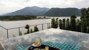 A glass-top infinity pool with a birdcage containing pastries, a glass of drink, and a wicker chair. - Pause pausa (Phrao)