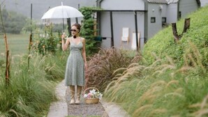 A woman in a dress standing on a path with a basket of flowers, holding an umbrella. - Pause pausa (Phrao)