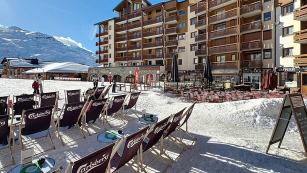 A ski resort with multiple-story buildings, outdoor seating areas, and a mountainous backdrop.
