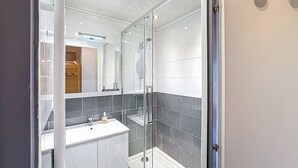 A modern bathroom with a glass shower enclosure, white vanity, and dark tiled walls.
